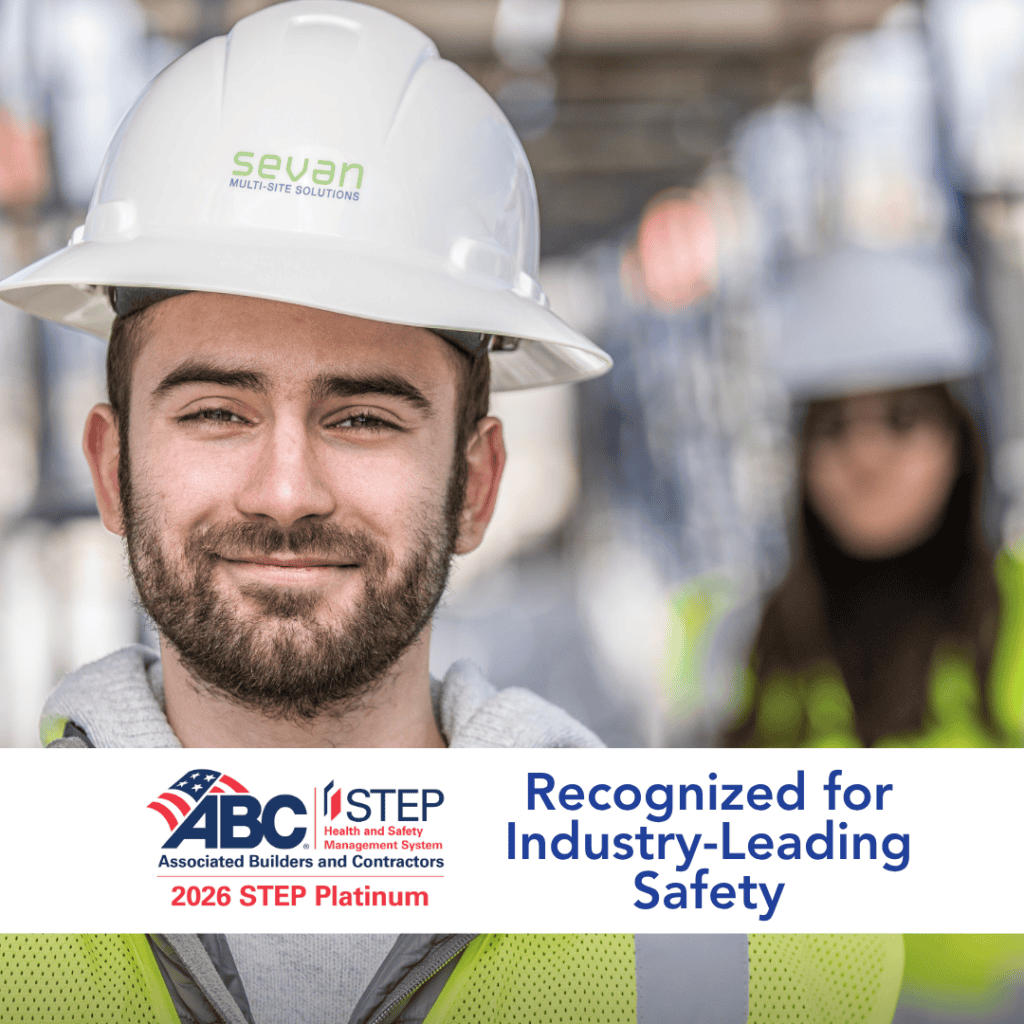 A construction worker in a hard hat and safety vest stands in focus, with another worker blurred in the background. Text highlights an industry safety recognition.