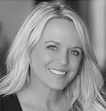 Smiling woman with long, light hair, wearing a necklace, photographed in black and white.