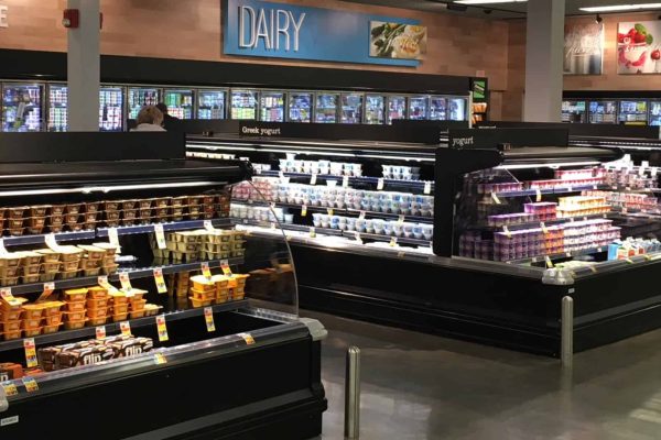 Grocery store dairy section with refrigerated shelves displaying various brands and types of yogurt.