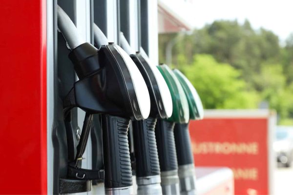 Close-up of four fuel pump nozzles at a gas station, with red and green handles, set against a blurred outdoor background.