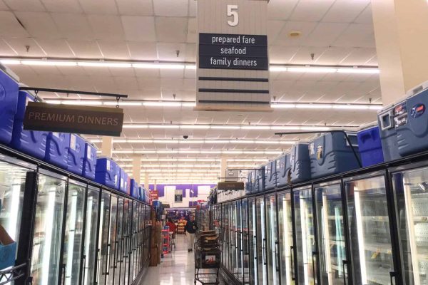 Grocery store aisle 5 with freezers on both sides, labeled for prepared fare, seafood, and family dinners; blue coolers are stacked above the freezers.