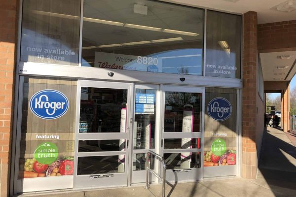 Entrance of a Kroger grocery store with sliding glass doors, store signs, and Simple Truth product advertisements on the windows.