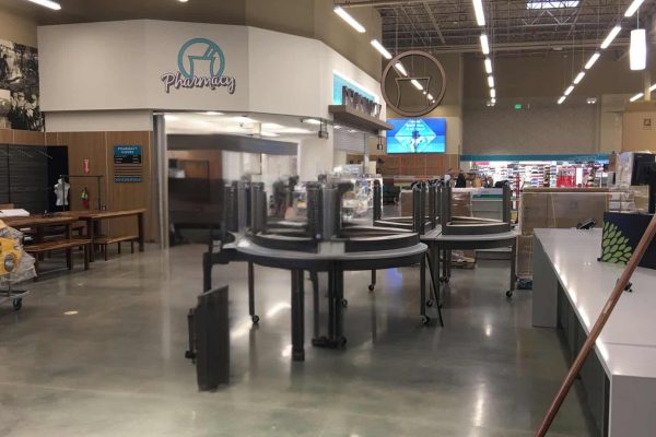 A grocery store interior with empty shelves, closed pharmacy, and unused display tables; the store appears to be under construction or recently opened.